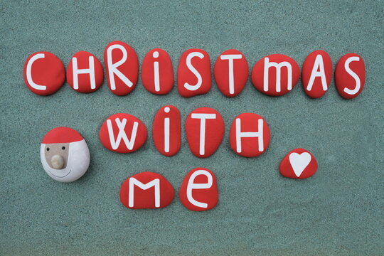 Christmas with me, creative text composed with hand painted red colored stone letters and a stone Santa Claus over green sand