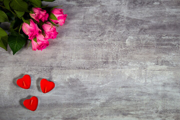 Closeup footage of pink roses and red candles in shape of heart lying on grey wooden surface filmed from above. Creative decoration for celebrating Valentines Day or romantic date. Theme of engagement