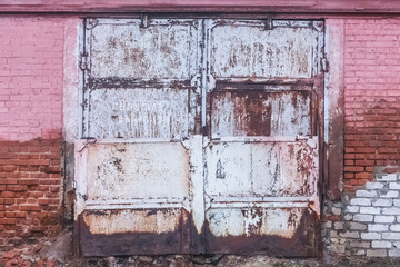 Naklejka premium Old dirty worn weathered iron warehouse door with brick wall of building abandoned architecture