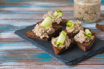 Appetizer, herring, onion and boiled egg forshmak on fried rye bread on a slate or stone board on a wooden background. Jewish cuisine.
