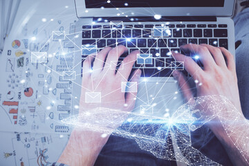 Double exposure of man's hands typing over computer keyboard and flying envelop hologram drawing. Top view. e-mail concept.