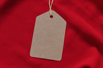 Price tag or blank cardboard label with thread isolated on the red cloth. Great for clothing or fashion mockups.