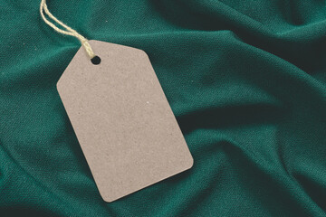 Price tag or blank cardboard label with thread isolated on the green cloth. Great for clothing or fashion mockups. fashion, etc.