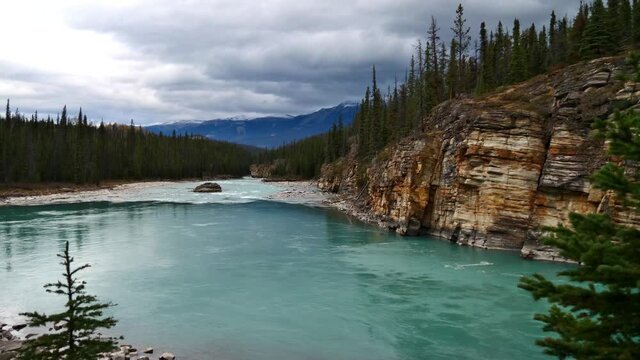 View of the wild Athabasca River near waterfall Athabasca Falls in Jasper National Park, Alberta, Canada in the Rocky Mountains on cloudy day in autumn season surrounded by eroded colorful rocks and f