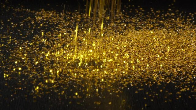 Gold dust, shimmer falls in black background and forms hill.