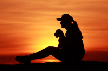 Silhouettes of a girl with a little beagle puppy on a sunset background