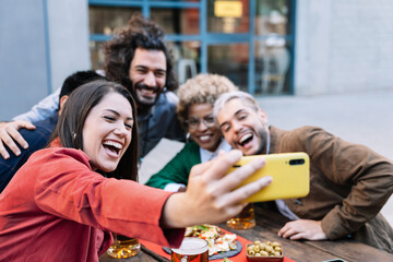 Young woman taking selfie photo of celebration with friends in outdoors bar to share on social media