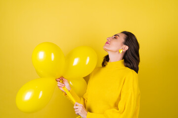 Young pretty woman in a yellow sweater on a background with balloons celebrates the best birthday of the thirtieth birthday