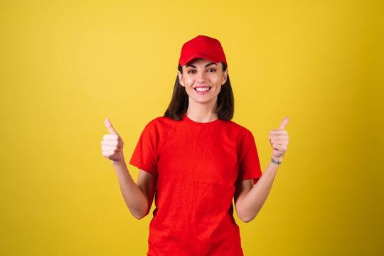 Delivery service worker woman in red cap, blank t-shirt, uniform, work clothes, courier at the service during quarantine, coronavirus covid-19 virus shows thumbs up