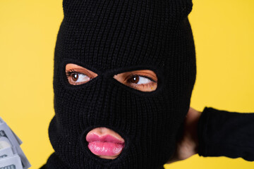 Young sexy beautiful woman with bright pink lips, balaclava on her head, holding a fan of 100 dollars, hacker, robbery, fraudster