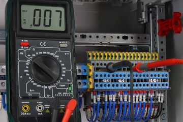 Measurement of electrical parameters using a multimeter in an electrical cabinet.