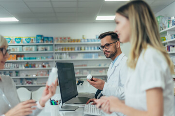 Male pharmacist working on a computer while female pharmacist is giving prescription medications to...