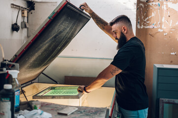 Male worker using a screen exposure unit while working in a printing workshop