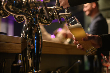 Hand of bartender using beer tap while working in a bar