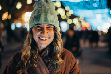 Portrait of a young smiling woman outside with the decorative christmas lights in the background