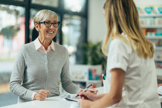 Happy senior woman customer buying medications at drugstore while talking with a female pharmacist