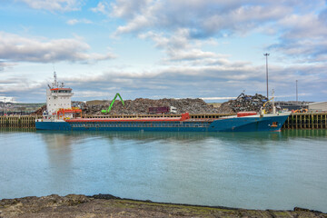 Ship moored in the harbour of Newhaven, UK, being loaded with scrap metal for export, out of the country. Lorry delivering more scrap meatal.
