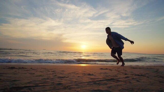 A male athlete is making back flip and lands on feet on the sandy tropical beach at sunset, slow motion