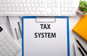 TAX SYSTEM written on the paper with keyboard, chart, calculator and notebook