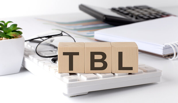 TBL written on a wooden cube on keyboard with office tools