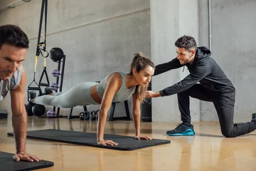 Fotobehang Personal trainer corrects woman's plank position at gym. © BASILICOSTUDIO STOCK