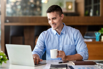 Businessman holding a coffee mug working on laptop at office.
