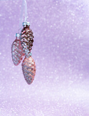Pink mother-of-pearl 3 cones hang from ribbons. Christmas card on a lilac shiny background.