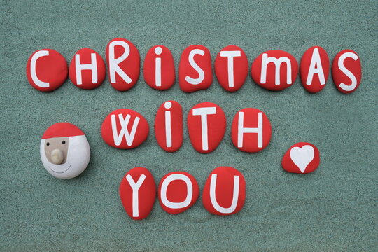 Christmas with you, creative text composed with hand painted red colored stone letters and a stone Santa Claus over green sand