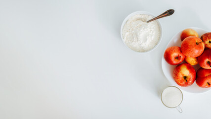 Ingredients for making pie at home. Red apples on plate on white table, top view. Banner with copy...