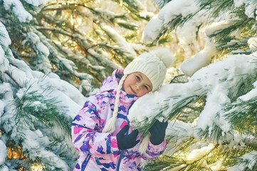 A little girl in a warm sports jacket on a winter walk in the woods