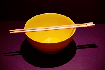 yellow porcelain rice bowl with wooden chopsticks on dark background
