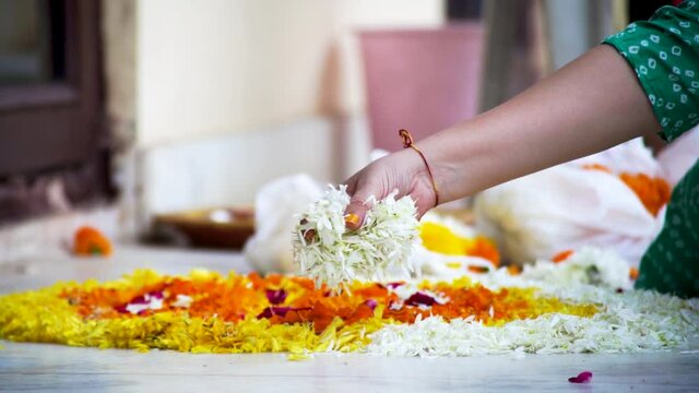 slow motion shot of Indian woman dropping marigold jasmine flowers on a rangoli pattern on the floor while making a rangoli for diwali, new year or a wedding decoration as part of the hindu religion