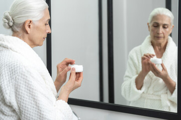 Aged woman with cream jar in front of mirror