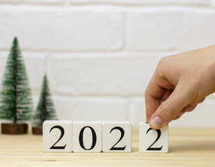 Happy New Year. A hand holds a wooden cube of the year 2022 word on a table background.