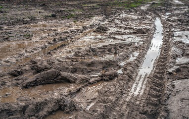 Wet clay field with wheel tracks and puddles of water. The photo was taken in the Dutch province of South Holland on a rainy day in the autumn season.