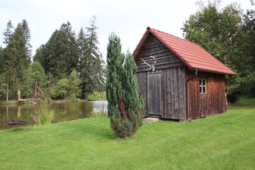 Obraz premium A beautiful wooden cottage near the small pond with trees around at Nova Bystrice, Czech republic