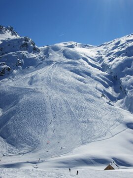 Long piste in the mountains. Skiers in snowy mountains. French alps. Les Sybelles ski area.