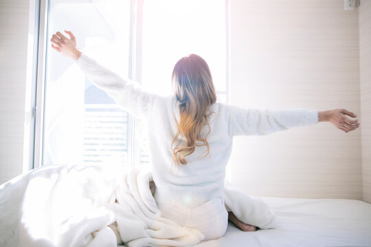 白い明るい部屋のベッドで朝日を浴びながらストレッチする女性