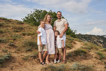 friendly family stands on the slope on a sunny summer day. mom is pregnant, two sons and dad.