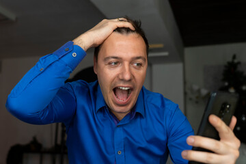 Surprised attractive man using internet on his mobile phone looking excited and shocked pulling hair. Funny businessman browsing telephone screaming in astonishment