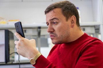 Surprised businessman looking at phone screen sitting at workplace in office. Shocked gasping man thinking of problem solution stuck with task. Confused guy reading news on phone with disgust