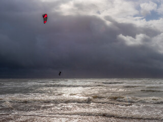 A kitesurfer surfing along the waves on a sandy beach against a cloudy and stormy sky in Wales