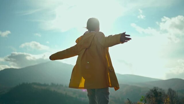 rear view slow motion b-roll Freedom woman with open arms enjoying beautiful landscape around mountains, standing against blue sky with sun and clouds