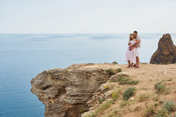 beautiful couple on the background of a beautiful seascape. a man hugs a pregnant woman from behind.