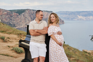old piano, on against the backdrop of a rocky sea coast. a pregnant woman and a man stand next to him and look at each other