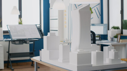 Close up of building model on table in empty architectural office. Nobody in workplace used for architecture project and urban property development. Blueprints and maquette on table