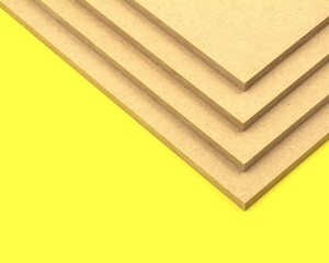 Raw mdf cut to size and stacked on top of each other, photographed on a yellow background.