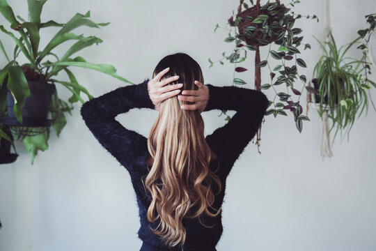 植物に囲まれた室内で手で髪を束ねる女性のポートレート