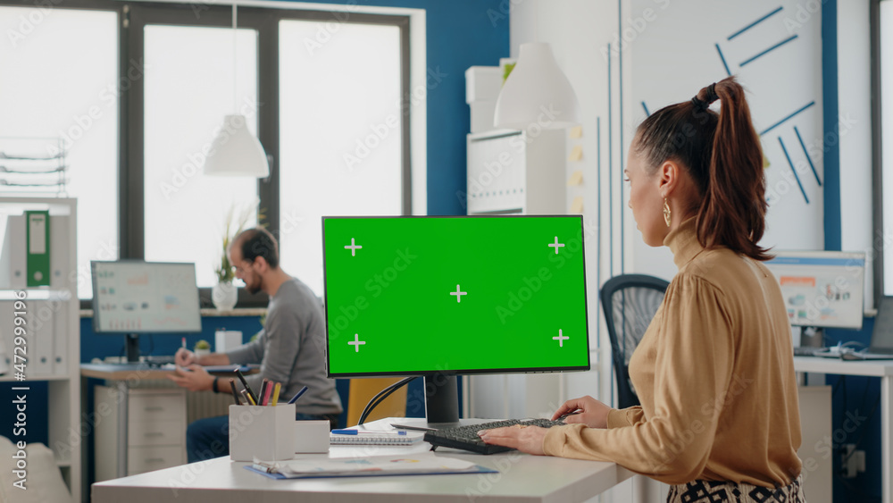 Poster woman working with isolated green screen on monitor at desk, looking at chroma key background with m