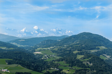 Fototapeta na wymiar Bergige Landschaft in Österreich. Blick von einem hochgelegenen Punkt auf eine Gebirgskette. und einen kleinen Ort im Tal. Sonniger Herbsttag